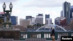 Seorang perempuan mengenakan masker, berjalan sendirian melintasi jembatan pusat kota yang luar biasa sepi pada hari pertama lockdown di Melbourne, negara bagian Victoria, Australia, di tengah pandemi COVID-19, 16 Juli 2021. (REUTERS/Sandra Sanders)