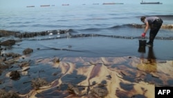 Foto ini diambil pada 2 April 2018 menunjukkan seorang polisi berusaha membersihkan Pantai Benua Patra setelah terjadi tumpahan minyak di dekatnya di Balikpapan. (Foto: AFP)