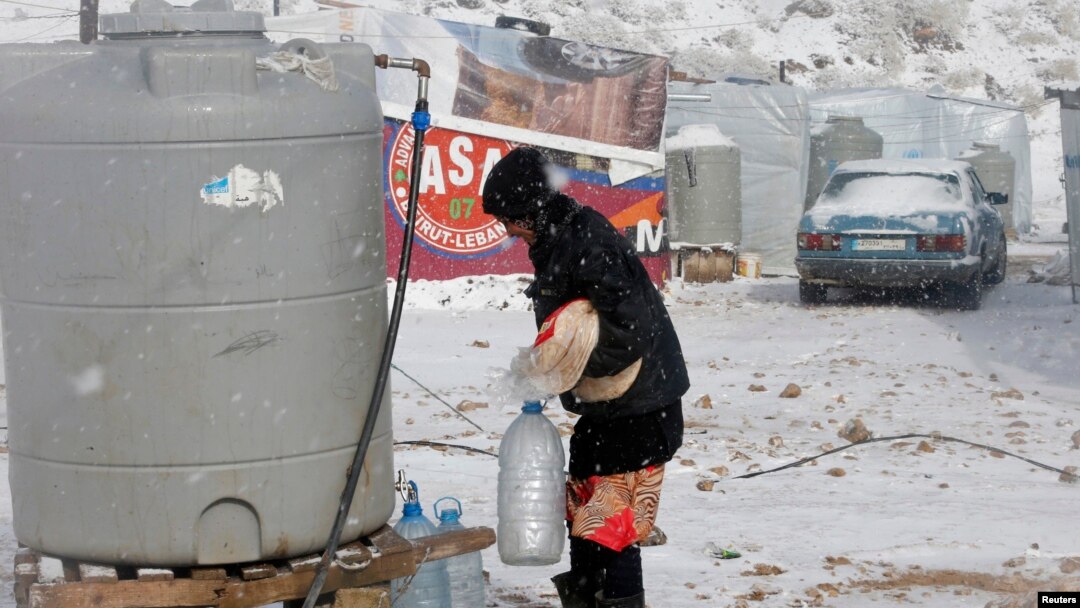Seorang pengungsi Suriah membawa roti dan botol-botol air di tengah badai salju di kota Zahle, Lebanon (11/12). (Reuters/Mohamed Azakir)