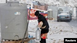 Seorang pengungsi Suriah membawa roti dan botol-botol air di tengah badai salju di kota Zahle, Lebanon (11/12). (Reuters/Mohamed Azakir)