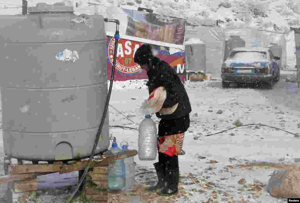 Seorang pengungsi Suriah membawa roti dan botol-botol berisi air di tengah badai salju di kota Zahle di lembah Bekaa, Lebanon timur (11/12). (Reuters/Mohamed Azakir)