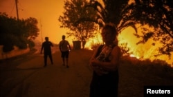 A local resident holds bottles of water near a wildfire burning in the village of Latas, in southern Greece, June 21, 2024.