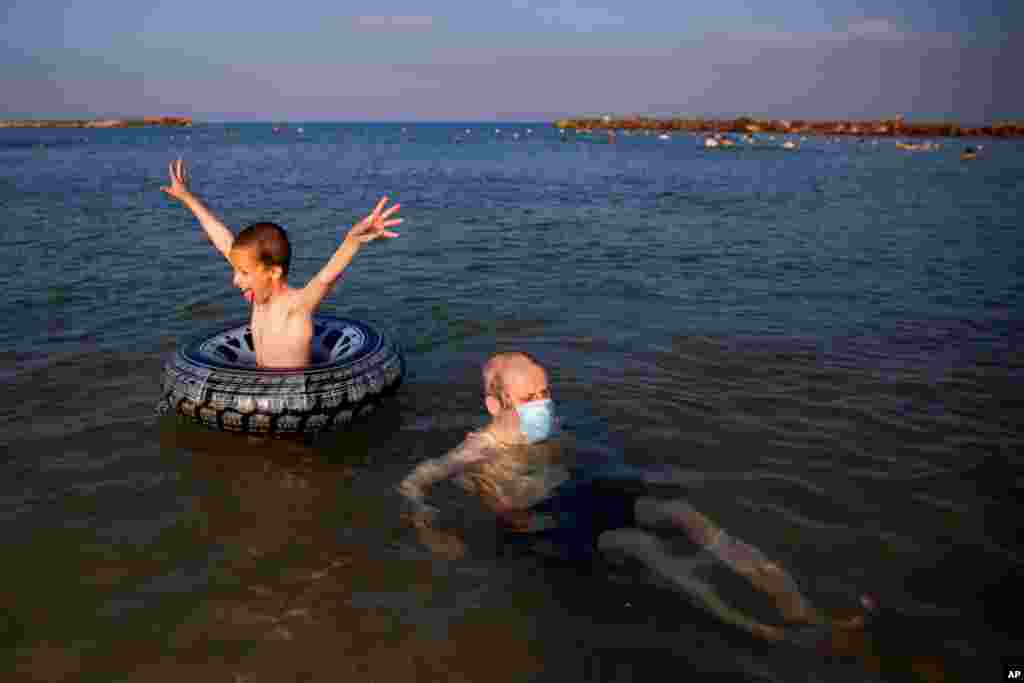 این پدر و پسر در حال لذت از تابستان در ساحل مدیترانه در شهر تل‌آویو اسرائیل. برخی مثل این پدر با ماسک در دریا حضور یافته‌اند. 