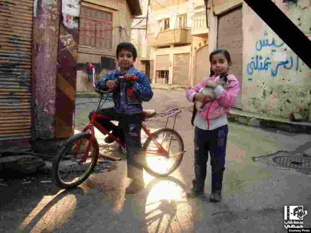 A Syrian boy and girl are seen posing for a photograph. Thirty minutes after the picture was taken a shell fired from a government-held position reportedly killed them both. Homs, January 20, 2013 (Lens Young Homsi)