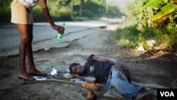 Una vecina ofrece agua a Antonio José, de 30años, tumbado en la carretera a las afueras de la capital.