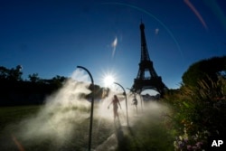 A spectator walks through water mist sprayers on her way to the Eiffel Tower Stadium to watch a beach volleyball match at the 2024 Summer Olympics, July 28, 2024, in Paris, France.