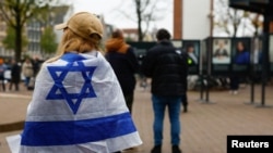 Seorang perempuan mengenakan bendera Israel berdiri di luar gedung di mana Wali Kota Amsterdam Femke Halsema menghadiri jumpa pers menyusul kekerasan yang menarget fans klub sepak bola Israel di Amsterdam, Belanda, Jumat, 8 November 2024. (Foto: Piroschka Van De Wouw/Reuters)