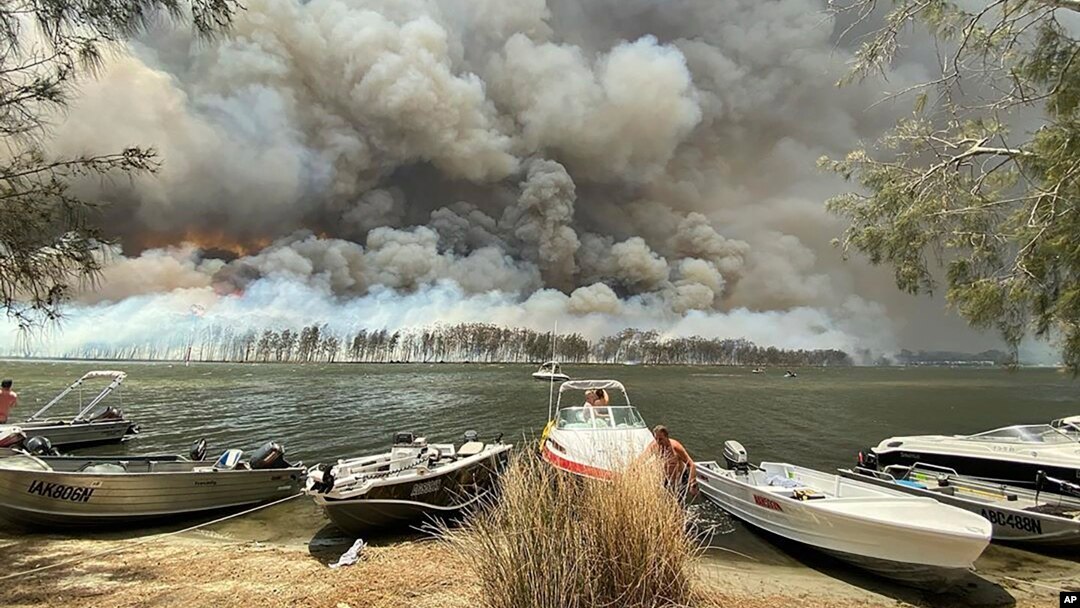 Kapal-kapal ditarik ke tepi danau saat asap tebal dan kebakaran hutan membumihanguskan kawasan di sekitar danau Conjola, Australia, Kamis, 2 Januari 2020.