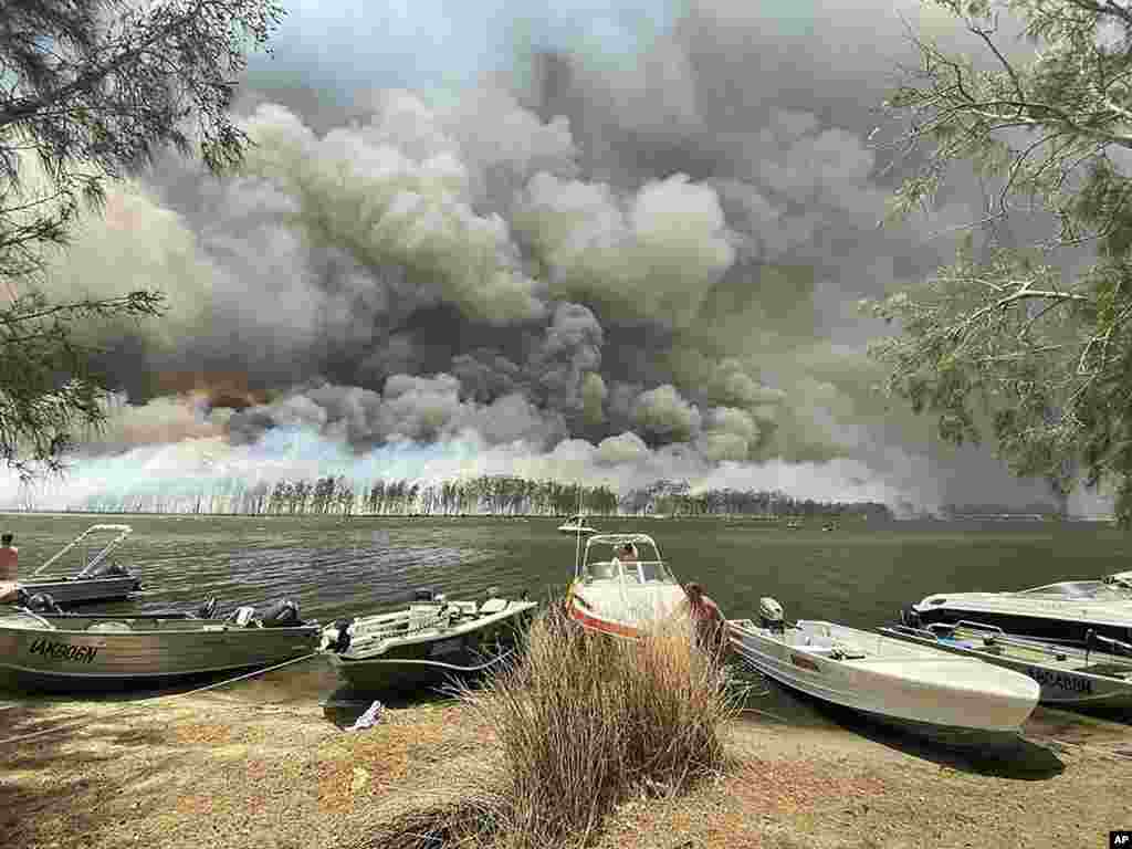 Boats are pulled ashore as smoke and wildfires rage behind Lake Conjola, Australia.