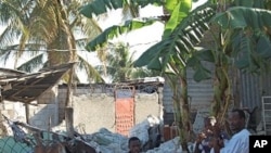 A family in the destroyed town of Carrefour, Haiti sits amid the charred rubble of their home, 25 Jan 2010