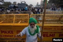 FILE - A farmer stands in front of police barricades during a protest against the newly passed farm bills at Singhu border near Delhi, India, Dec. 3, 2020.