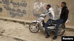 Des chômeurs assis sur une moto dans le quartier pauvre de Zhor, à Kasserine. Sur le mur, on peut lire un graffiti «Jeunes marginaux».