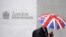 FILE - A worker shelters from the rain as he passes the London Stock Exchange in the City of London at lunchtime, Oct. 1, 2008. 