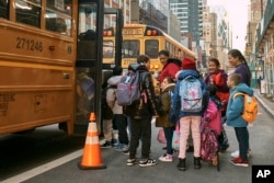 FILE - Migrant kids take a school bus watched by their guardians in front of the Row Hotel that serves as migrant shelter on Tuesday, Dec. 12, 2023, in New York. (AP Photo/Andres Kudacki)