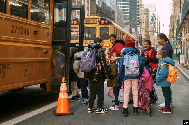 FILE - Migrant kids take a school bus watched by their guardians in front of the Row Hotel that serves as migrant shelter on Tuesday, Dec. 12, 2023, in New York. (AP Photo/Andres Kudacki)