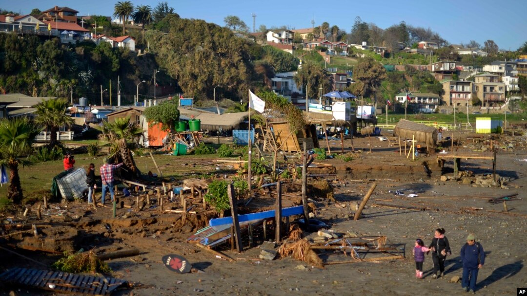People walk past destroyed surfing schools on the beach after an earthquake-triggered tsunami in Concon, Chile, Sept. 17, 2015.