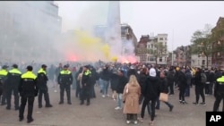 En esta imagen tomada de un video, la policía hace guardia mientras los partidarios del Maccabi Tel Aviv encienden bengalas en la plaza Dam, en Ámsterdam, Países Bajos, el 7 de noviembre de 2024.