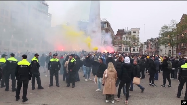 En esta imagen tomada de un video, la policía hace guardia mientras los partidarios del Maccabi Tel Aviv encienden bengalas en la plaza Dam, en Ámsterdam, Países Bajos, el 7 de noviembre de 2024.