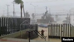 A woman walks under her umbrella while a car moves along a flooded road during Hurricane Genevieve in Los Cabos, Baja California Del Sur, Mexico, Aug. 19, 2020, in this still image obtained from video provided on social media. 