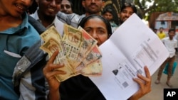 FILE- An Indian woman shows discontinued Indian currency notes and copy of photo identity card as she stands in queue outside Reserve Bank of India to deposit and exchange them in Ahmedabad, India, Nov. 17, 2016. 