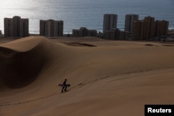 A man walks on ‘Cerro Dragon' nature sanctuary dune while practicing sandboard with Iquique city in the background, at Atacama desert, Iquique, Chile, Oct. 29, 2024.