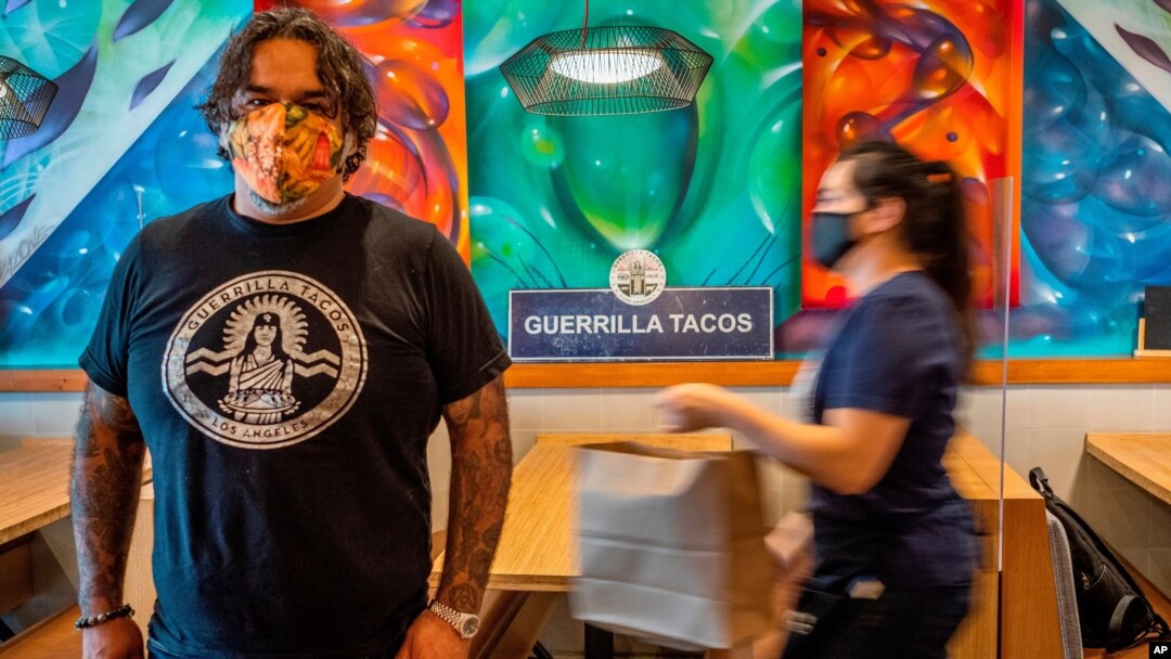 Guerrilla Tacos chef-owner Wes Avila poses for a picture as an employee in a face mask delivers to-go orders at his critically acclaimed restaurant in Los Angeles, July 3, 2020.