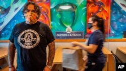 Guerrilla Tacos chef-owner Wes Avila poses for a picture as an employee in a face mask delivers to-go orders at his critically acclaimed restaurant in Los Angeles, July 3, 2020.