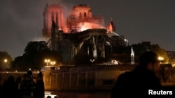 Firefighters douse flames from the burning Notre Dame Cathedral as people look on in Paris, France, April 15, 2019.