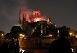FILE - Firefighters douse flames from the burning Notre Dame Cathedral as people look on in Paris, France, April 15, 2019.