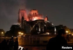 FILE - Firefighters douse flames from the burning Notre Dame Cathedral as people look on in Paris, France, April 15, 2019.