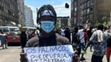 Um jovem com uma máscara a dizer “Povo no Poder” segura um cartaz a dizer “Os palhaços que deviam entreter as crianças governam o país”. Ele participa num protesto na cidade de Maputo