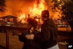 People watch as the Eaton Fire engulfs a structure in Altadena, California, Jan. 8, 2025.