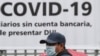 FILE - A man wears a face mask against the spread of the new coronavirus (COVID-19) as he waits to enter a bank to receive a $300 USD bonus, granted by the government for vulnerable people, in Santa Tecla, El Salvador, April 3, 2020.