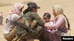 Displaced people from the minority Yazidi sect, fleeing violence from forces loyal to the Islamic State in Sinjar town, get help from a member of the YPG near the Syrian border.