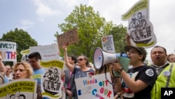 FILE - Protesters near the Morrelly Homeland Security Center, May 23, 2018, in Bethpage, N.Y. demonstrate against the immigration policies of President Donald Trump who is speaking to Homeland Security and law enforcement personnel. 