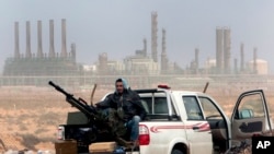 FILE - In this March 5, 2011 file photo, an anti-government rebel sits with an anti-aircraft weapon in front an oil refinery in Ras Lanouf, eastern Libya.