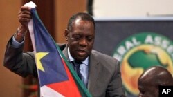 Confederation of African Football (CAF) president Issa Hayatou, left, receives South Sudan's national flag from its federation president Oliver Benjamin, right, during the Confederation of African Football General Assembly in Libreville, Gabon, Friday Feb