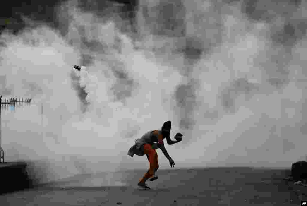 A Kashmiri demonstrator throws a tear smoke shell on government forces to protest against the Sunday&#39;s killing of a young man in Srinagar, Indian-controlled Kashmir.