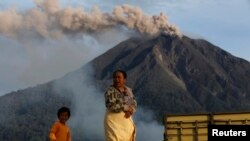 Seorang ibu berjalan sementara Gunung Sinabung memuntahkan debu, 29 November 2013. 