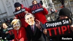 Protesters wear masks of U.S. President Barack Obama and German Chancellor Angela Merkel as they demonstrate against the Transatlantic Trade and Investment Partnership (T-TIP) free trade pact at the Hannover Messe in Hannover, Germany, April 24, 2016. 