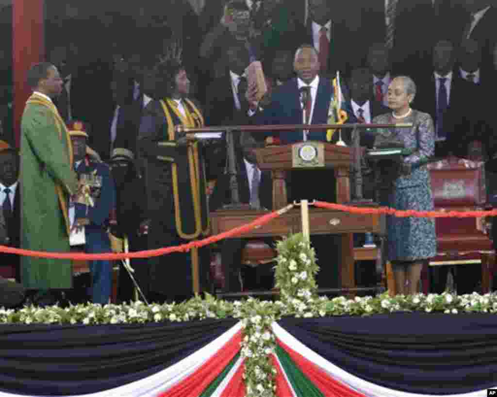 Madaxweyne Uhuru Kenyatta oo gacanta ku haya bible iyadoo loo dhaarinayo xilka madaxweynaha 4aad ee Jamhuuriyadda Kenya waxaana hareer taagan xaaskiisa Margaret Uhuru.