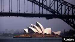 FILE - The sun illuminates the Sydney Opera House as a ferry sails past during a storm at Sydney Harbor in Australia.