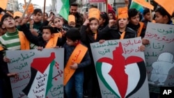 Protesters hold placards as others wave their national flags during a protest against the Mideast plan announced by the U.S. President Donald Trump, at Jebaliya refugee camp, Gaza Strip, Jan. 30, 2020. 