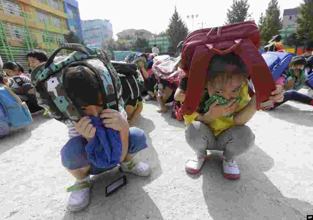 Elementary school students, with schoolbags on their heads, take shelter on the ground during an earthquake drill at Songjung Elementary School in Seoul, South Korea.