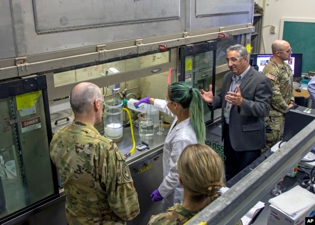 This September 2022, image provided by Los Alamos National Laboratory shows Lt. Gen. Thomas Bussiere, left, and James Owen, right, watch as scientist Bi Nguyen demonstrates the wet slurry formulation process in Los Alamos, N.M. (Los Alamos National Laboratory via AP)