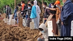 Seorang anak mendoakan anggota keluarga lainnya yang sudah dikuburkan di pemakaman khusus COVID-19 TPU Rorotan, Jakarta Utara. 8 Juli 2021 . (Foto:VOA/Indra Yoga)