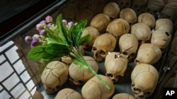 FILE - Flowers are laid on top of a glass case containing the skulls of some of those who were slaughtered during the 1994 genocide, in Ntarama, Rwanda, April 5, 2019.