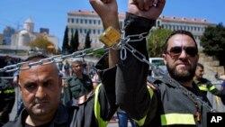 FILE - Civil Defense volunteers with symbolic metal chains around their wrists protest in front of the government building during a sit-in to demand full time jobs in fixed posts in Beirut, Lebanon, April 4, 2019.