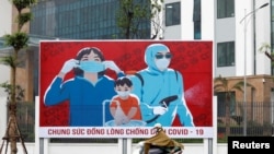 A man wears protective mask as he rides past a propaganda banner promoting prevention against the coronavirus disease (COVID-19) in Hanoi, Vietnam, April 3, 2020. 