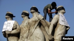 FILE- A student activist puts black scarves on the eyes of Shoparjito Shadhinota, a sculpture that represented all sections of people in Bangladesh's liberation War in 1971, demanding capital punishment for Bangladesh's Jamaat-e-Islami senior leader Abdul Quader Mollah, after a war crimes tribunal sentenced him to life imprisonment, in the campus of University of Dhaka, Feb. 6, 2013.